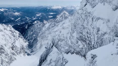 Aerial view of beautiful Bavarian Alps with town visible at the bottom of the mountain. camera rising and panning right as it reaches the summit and reveals a gondola station.