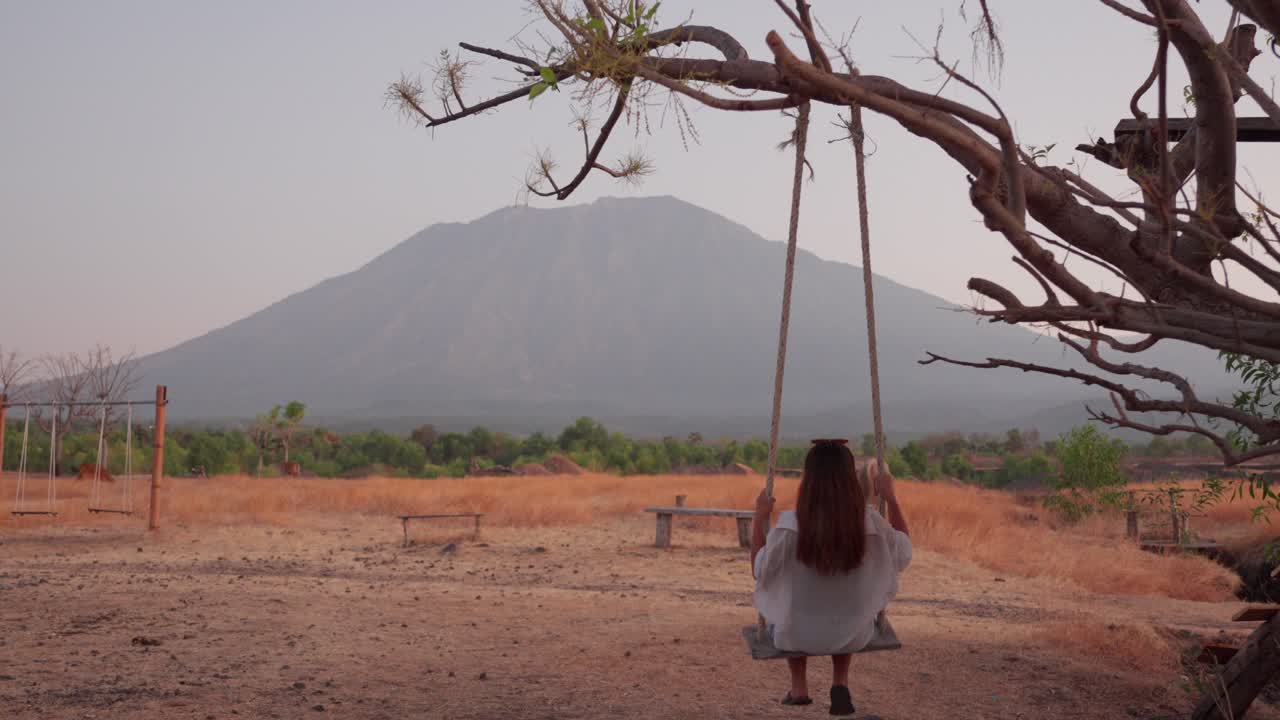Giovane donna su un'altalena in un deserto con il Monte Agung sullo sfondo.