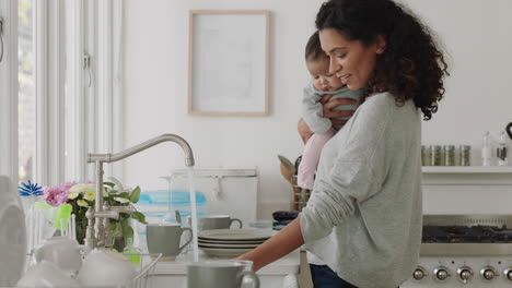 happy mother holding baby working at home washing dishes cleaning kitchen caring for toddler doing housework enjoying motherhood