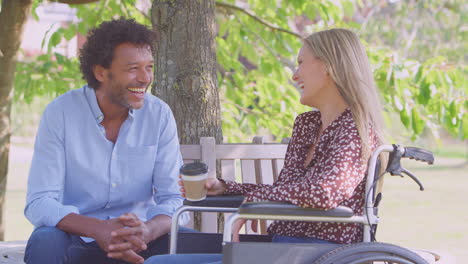 mature couple with woman sitting in wheelchair talking and drinking coffee in park together