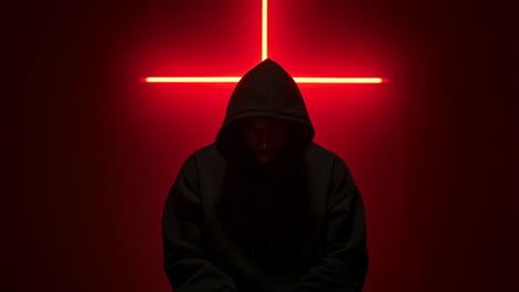 person in dark hoodie against red inverted cross