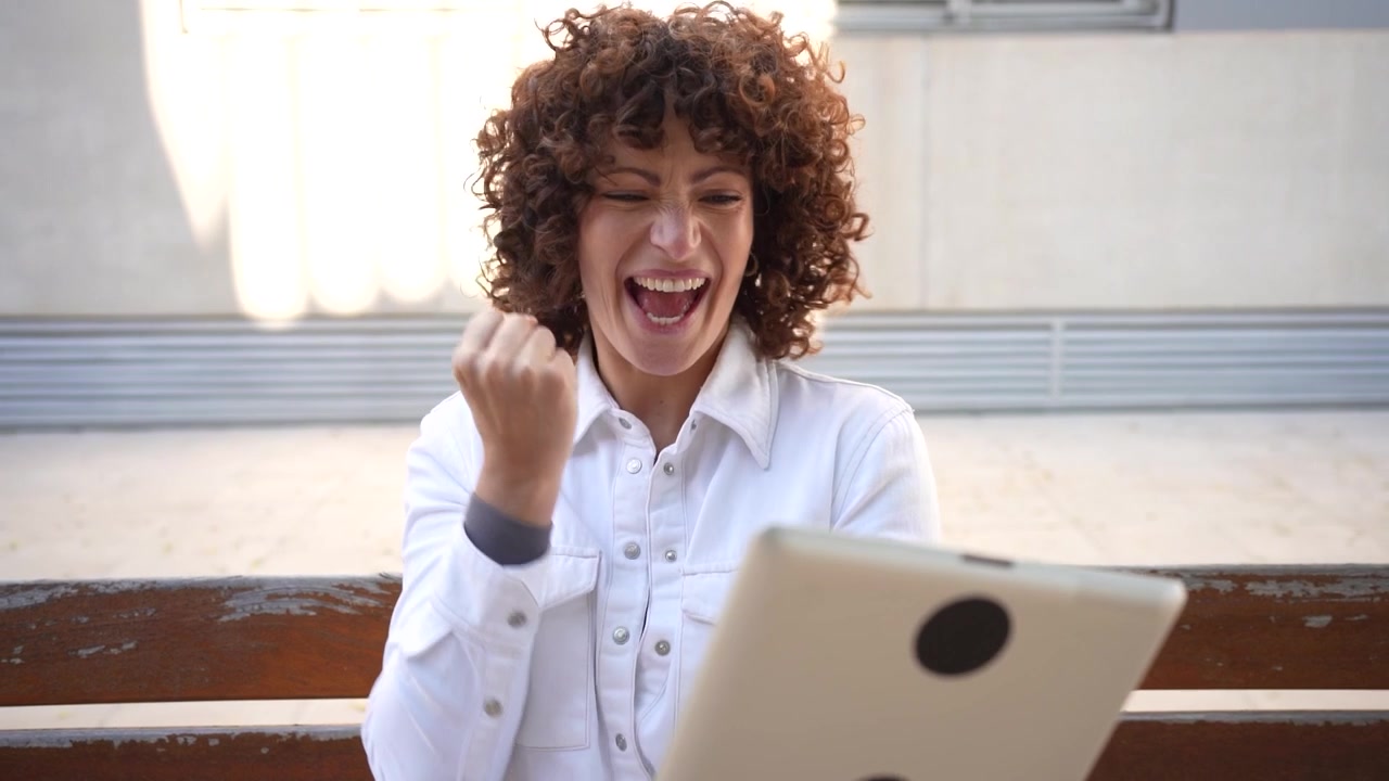 Una giovane donna è profondamente assorta nel suo tablet mentre è seduta in un piacevole ambiente esterno.
