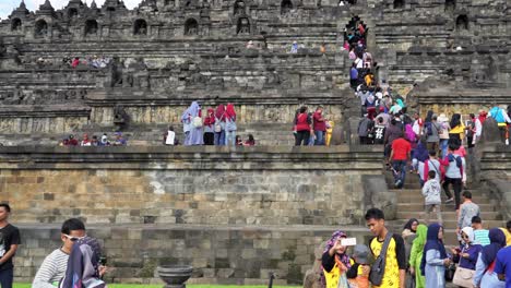 indonesia, jawa island,yogyakarta, unesco world heritage borobudur temple from outside,slow motion,people in motion around the temple complex on a cloudy day. some people posing,taking photos,climbing