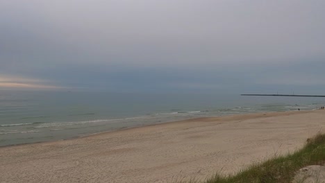 calm baltic sea waves wash onto the sandy shore of smiltynė under a moody overcast sky.