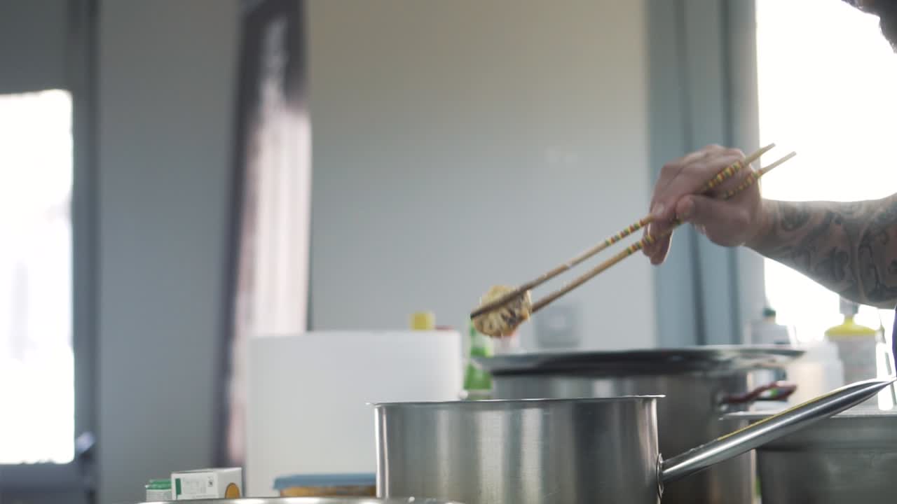 Master chef frying mushrooms in hot oil using chopsticks in close up view
