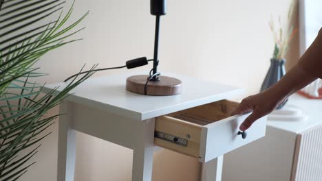 pessoa abrindo gaveta de uma mesa de noite branca com uma lâmpada preta
