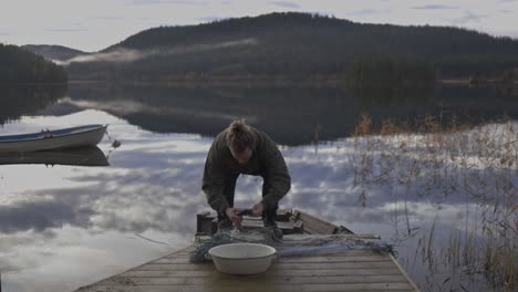 Man-Puts-The-Catch-Fish-Into-The-Basin-From-Fishing-Net-On-The-Wooden-Jetty