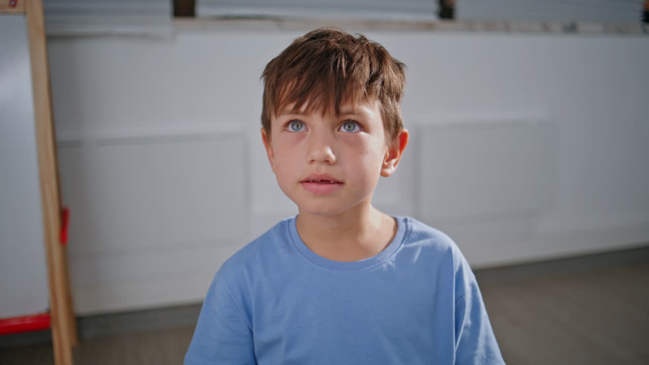 Little boy sitting school showing funny faces in classroom portrait. Funny pupil