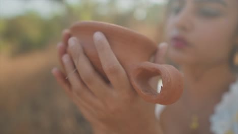 un primer plano abstracto de una mujer asiática acunando y admirando los detalles de una olla de arcilla mientras se sienta al aire libre disfrutando tranquilamente de su afición a la cerámica en la naturaleza, india