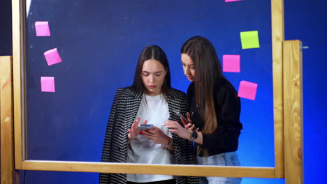A couple of two long-haired women look at the phone. Concentrated ladies are searching information or watching video.