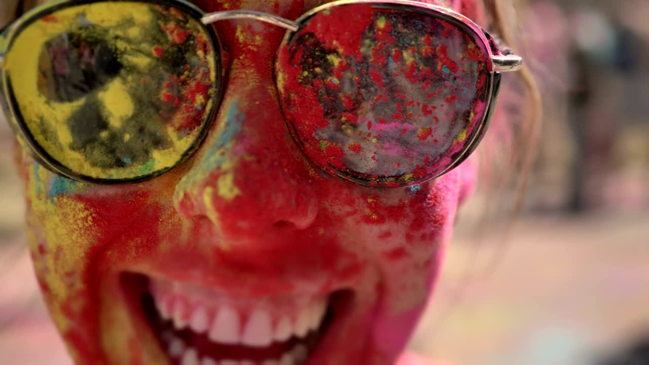 Face of young happy girl in colourful powder with sunglasses is smiling on holi festival in daytime in summer, color concept, emotional concept