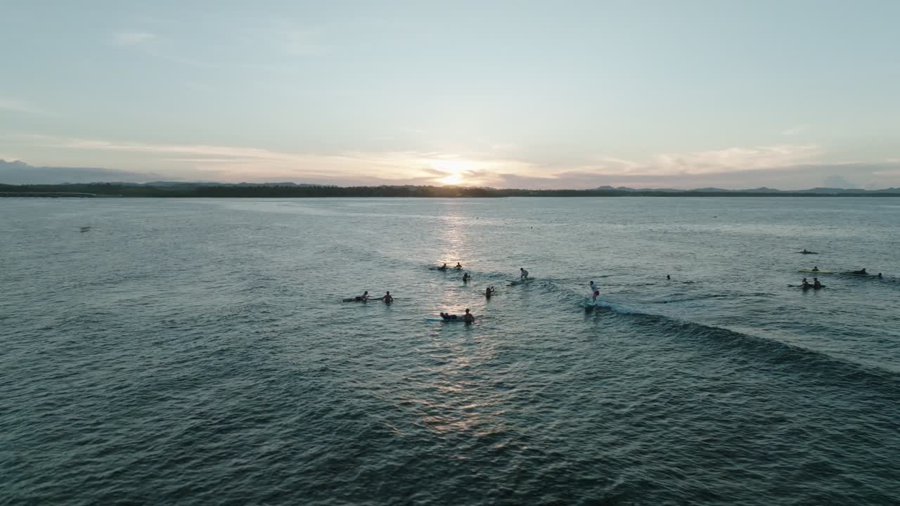 Smuk droneoptagelse fra luften af en surfer, der rider på en bølge ved solnedgang i General Luna, Siargao, Filippinerne. Sollys fra den gyldne time reflekteres på det tropiske havvand blandt en fredelig række surfere.