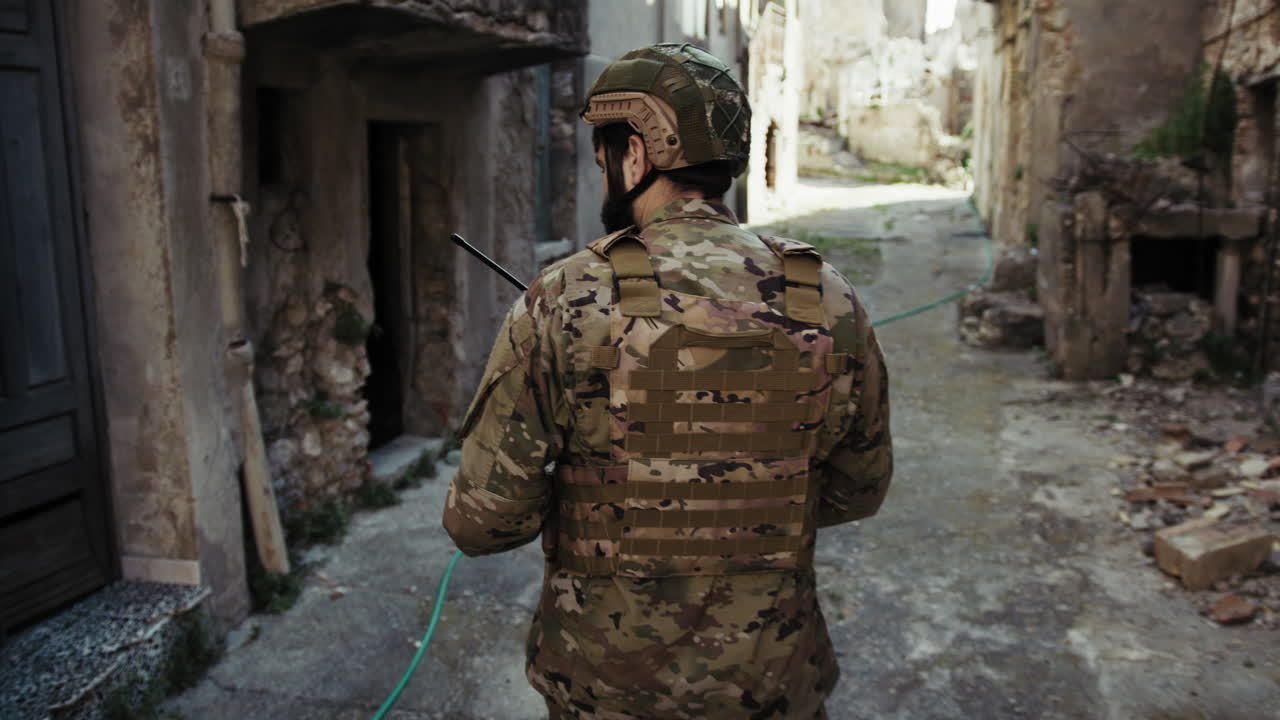 Young Soldier Walks Doing Reconnaissance In The Village Destroyed Streets