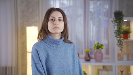 Unhappy-and-thoughtful-young-woman-standing-at-home-looking-at-camera-and-being-serious.