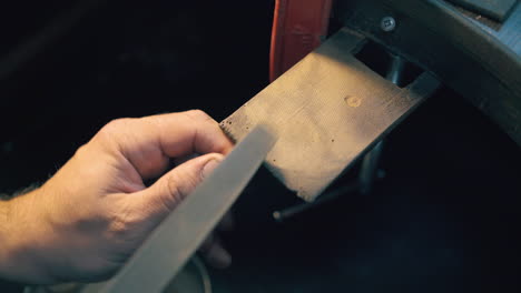 jeweler polishes gold bar with rasp at workplace closeup