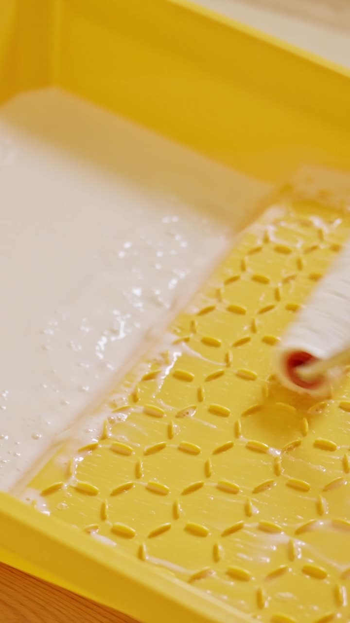 Vertical static shot shows a paint roller being saturated with primer inside a yellow tray, part of the hardwood floor preparation process to ensure better adhesion and smoother varnish application