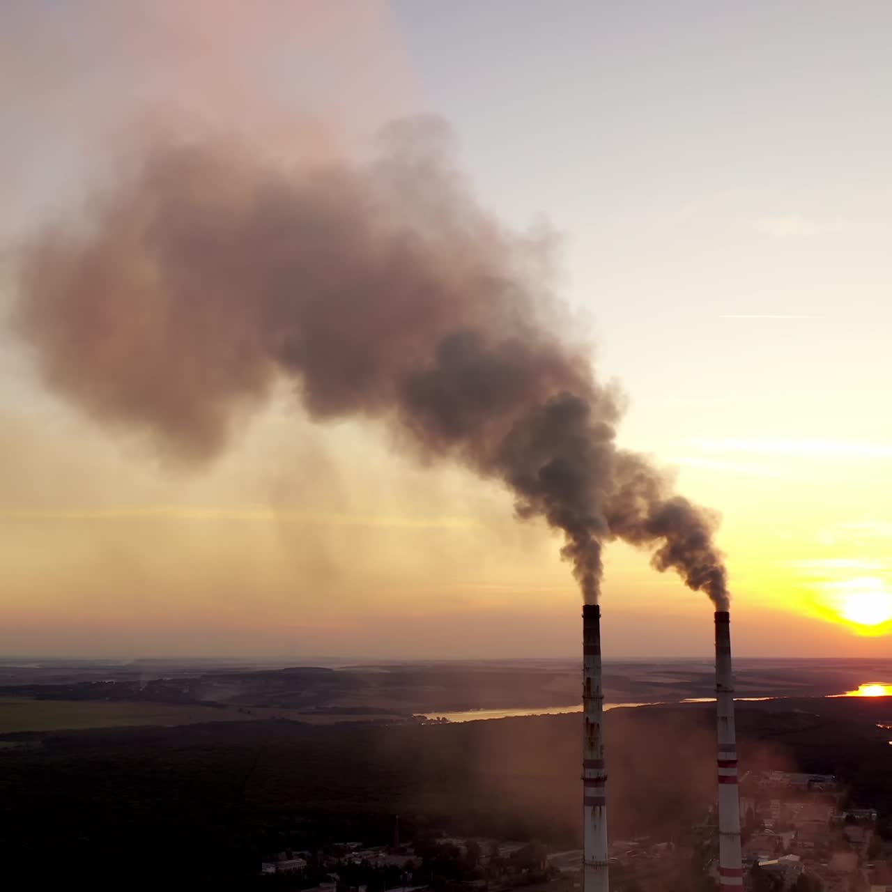 Environment pollution. Dark smoke going from two industrial pipes on nature background at sunset.