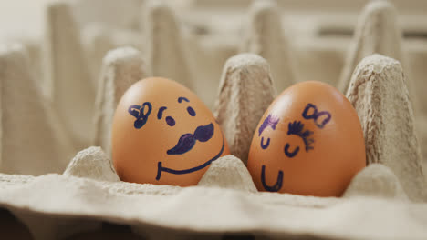 video of close up of two brown eggs with drawn faces in egg carton background