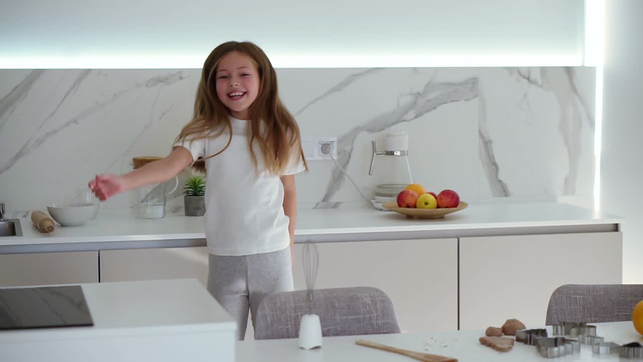 Happy beautiful little girl dancing in modern kitchen having fun doing funny dance moves. Long haired, smiling girl enjoying weekend at home. Slow motion