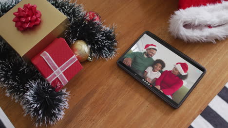 sonriente familia afroamericana con sombreros de santa claus en la videollamada de navidad en la tableta