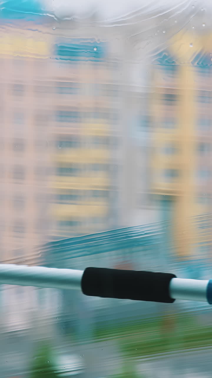 Cleaning dirty window with solution. Worker using household brush to wash window with special liquid inside. Blurred multi-storey building backdrop. Vertical video