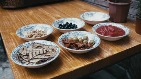 pizza ingredients layed out in plates on wooden table