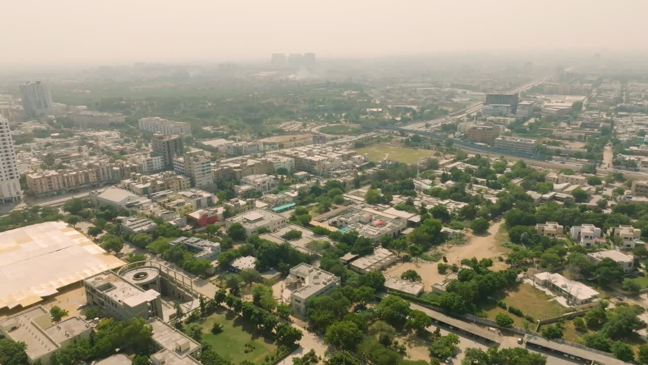 High altitude wide-angle drone footage over NED University in Karachi, capturing the campus architecture against a backdrop of the city skyline fading into atmospheric haze