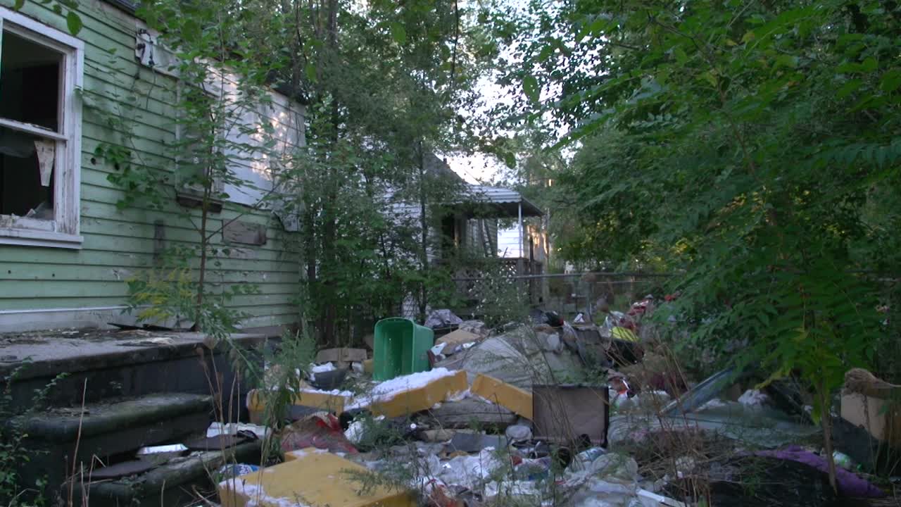 Large amount of garbage lies in the backyard of a dilapidated chalet with broken windows among the greenery in Detroit. Slowly zooming shot