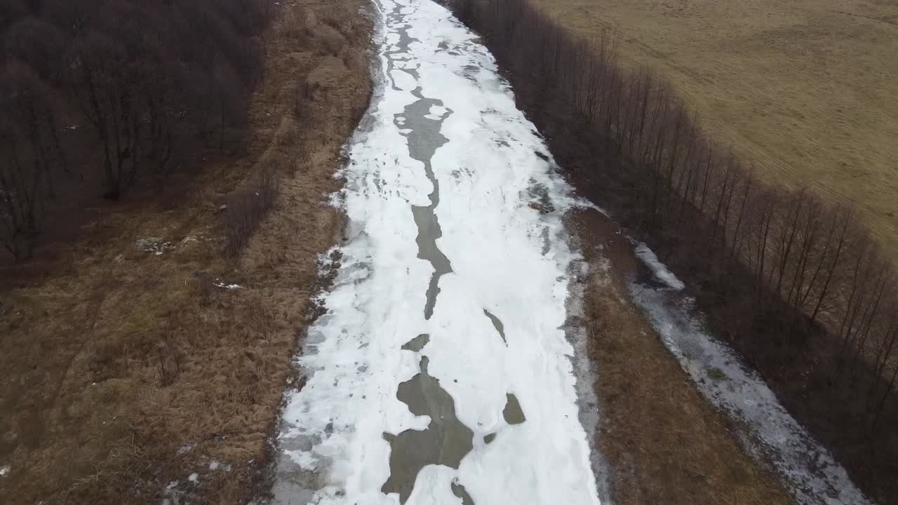 Съемка с дрона: лес и замерзшая загородная река поздней осенью.
