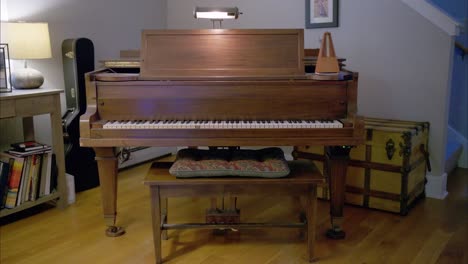 a vintage wooden piano in a living room with an antique mechanical metronome swinging at 60bpm on the right, a guitar case and rustic trunk in the back