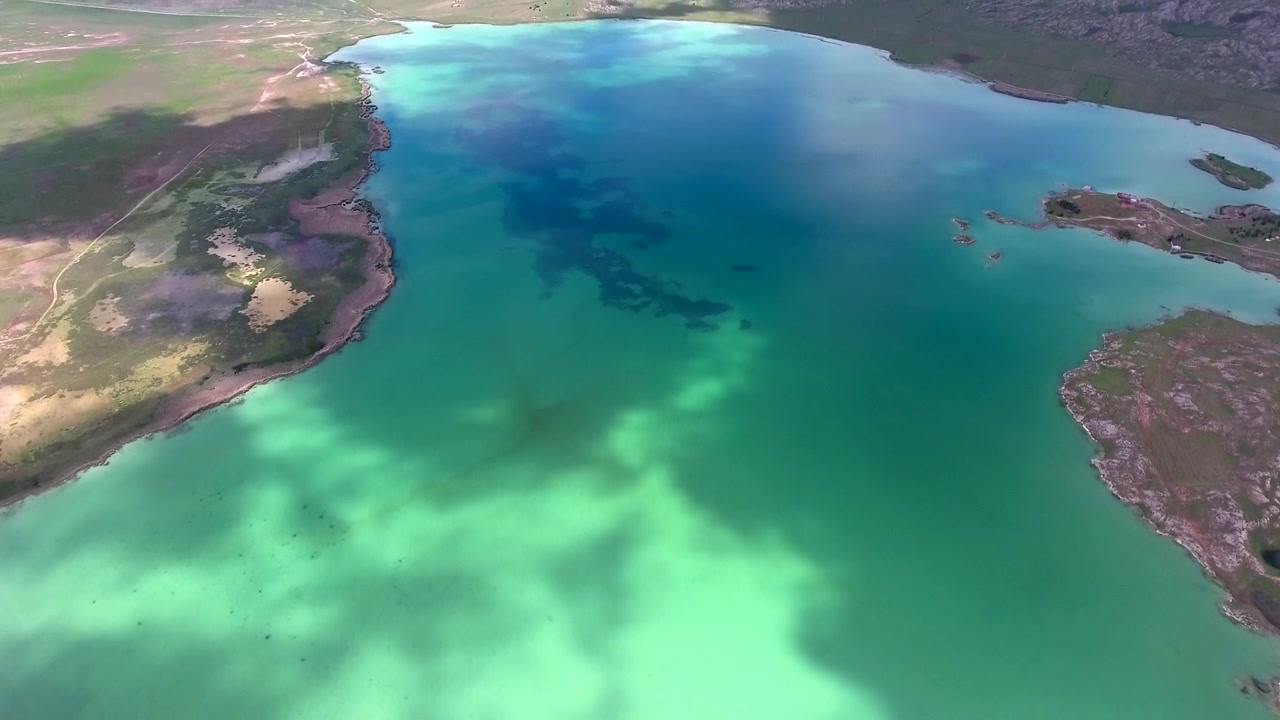 Luftfoto av en turkis innsjø med skyggespill fra skyer