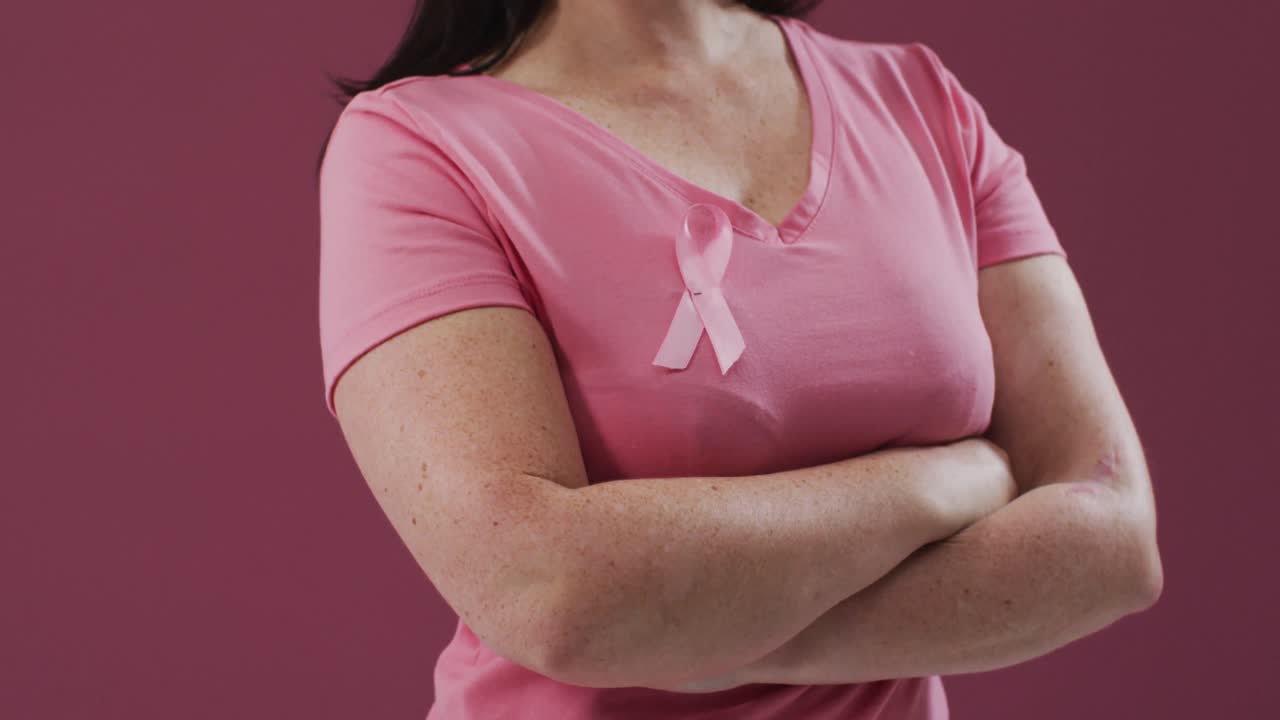 Donna con le braccia incrociate che indossa un nastro rosa per la consapevolezza del cancro sulla maglietta.