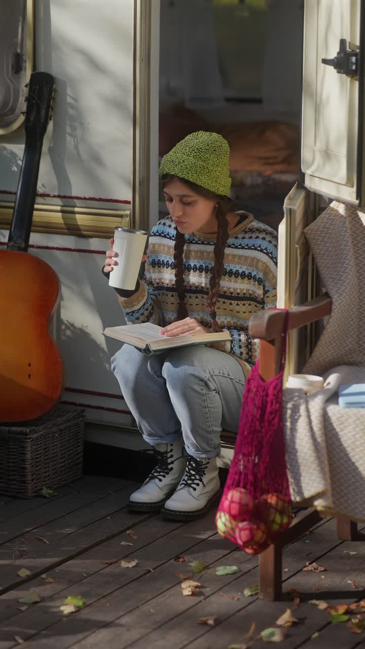 Donna che legge un libro sorseggiando una bevanda in un camper