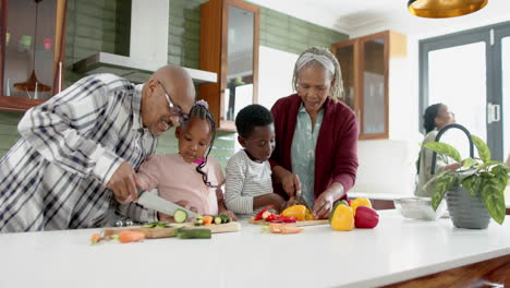 Happy-african-american-grandparents-and-grandchildren-chopping-vegetables-in-kitchen,-slow-motion