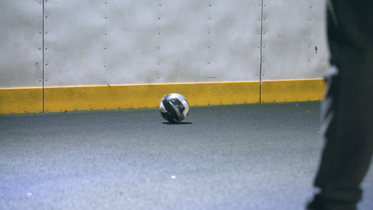 야간에 밝은 조명 아래 벽에 축구공을 는 운동복을 입은 다리의 클로즈업, 집중된 도시 스포츠 설정으로 움직임, 에너지 및 그림자를 강조합니다.