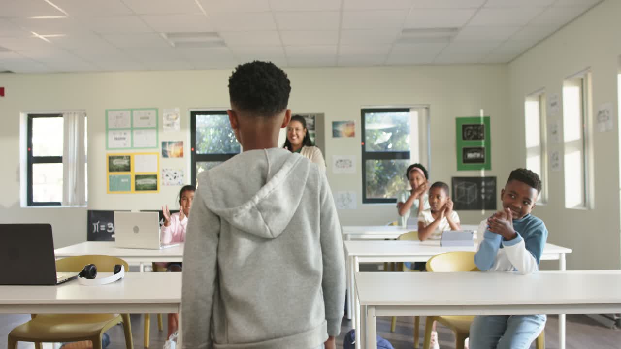 Classe afro-américaine applaudissant en classe, professeur avec une tablette encourageant un garçon préadolescent à s’incliner et à marcher