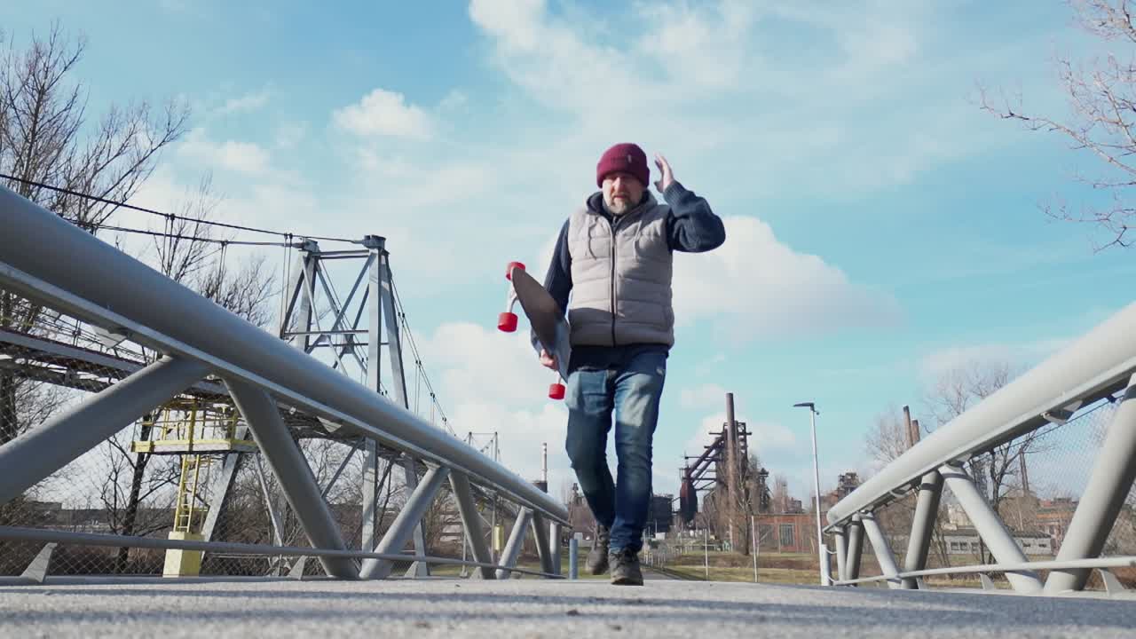 Elderly person walking on a metal bridge, holding a longboard