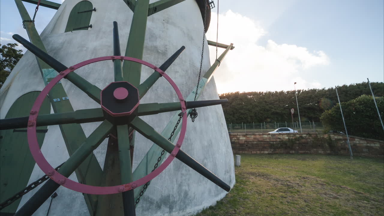 A scenic time-lapse view of a classic windmill on a sunny day, showcasing its architectural details and the surrounding landscape. The sky has some nice clouds