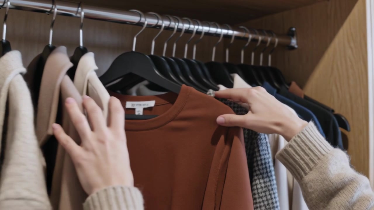 Mani e avambracci che si allungano per selezionare cappotti sull'asta dell'armadio, scegliendo l'outfit, mostrando i polsini del maglione