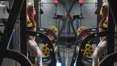 beautiful girl in the gym is squatting with a barbell. strength exercises for the feet. reflection in the mirror