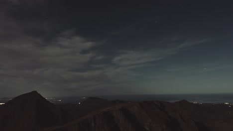 Beautiful time lapse of a night sky filled with stars in Norway, watching over mountains and city lights in the background