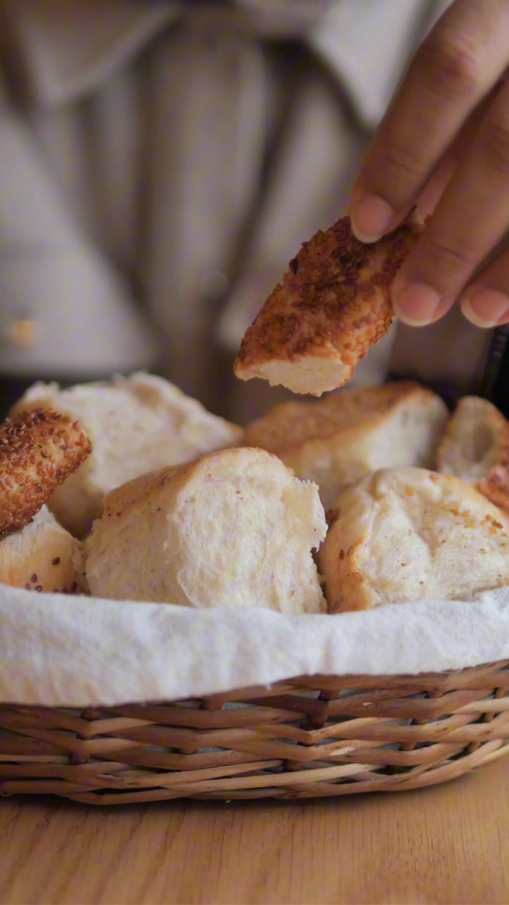 Hand Picking a Sesame Seed Bread Roll from a Basket