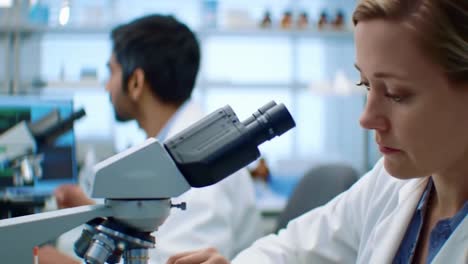 focused female scientist in a lab coat examines samples through a microscope