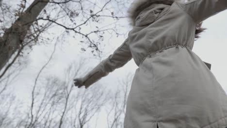 chica caucásica girando con los brazos abiertos en el bosque, slomo