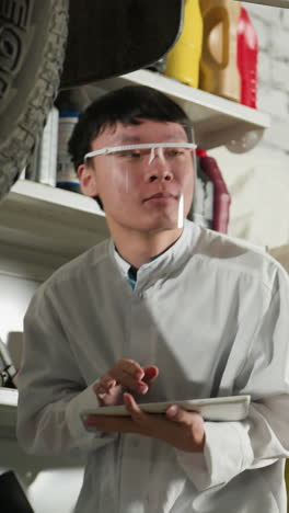 técnico de laboratorio con escudo facial observa un coche levantado en el taller, sosteniendo una tableta para el análisis técnico, características de fondo equipos mecánicos, herramientas industriales, llaves y estación de reparación
