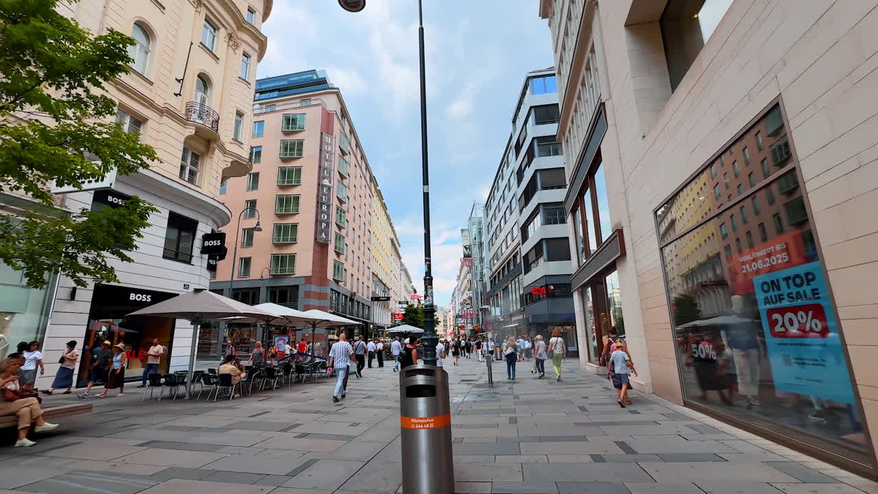 Vienna, Austria - June 9, 2025: Tourists and locals walk by the wide pedestrian street with multiple shops. Shopping in Vienna, Austria