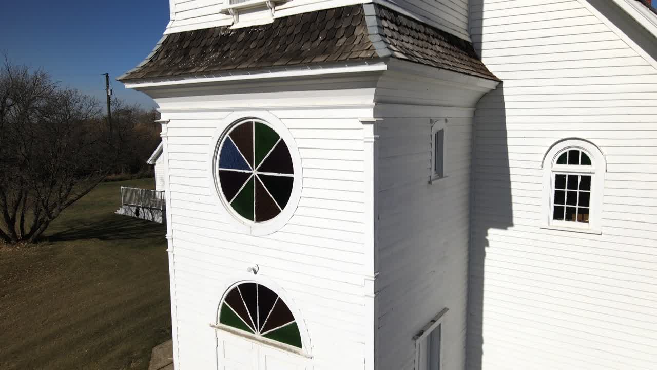 Close-up aerial shot of St Boniface catholic church in Spring Lake, Alberta on a sunny day. Drone ascending and showing countryside landscape behind the old wooden building. 4k cinematic reveal