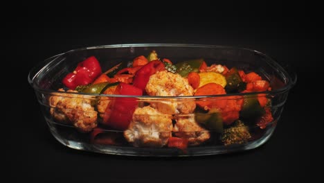 medley of grilled vegetables in a glass dish against black background