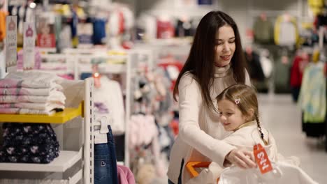 Madre-E-Hija-Caminando-Por-Una-Tienda-De-Ropa-Con-Una-Chica-En-Un-Carrito-De-Compras