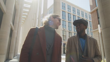 two cheerful multiethnic businessmen walking outdoors and speaking